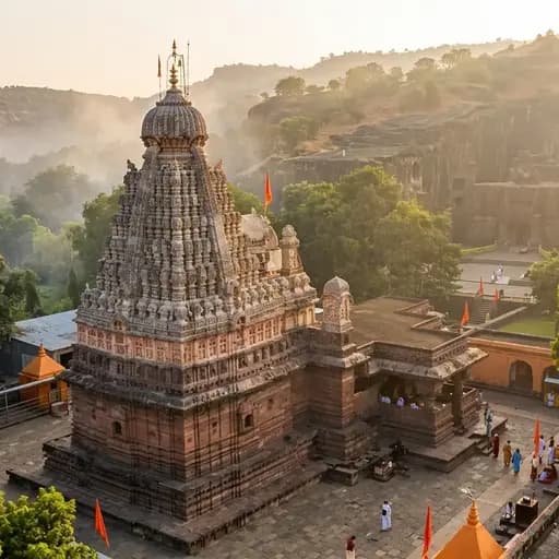Finely carved red basalt stone shikhara of Grishneshwar Jyotirlinga temple standing under a golden dusk sky near the ancient rock cliffs of Ellora